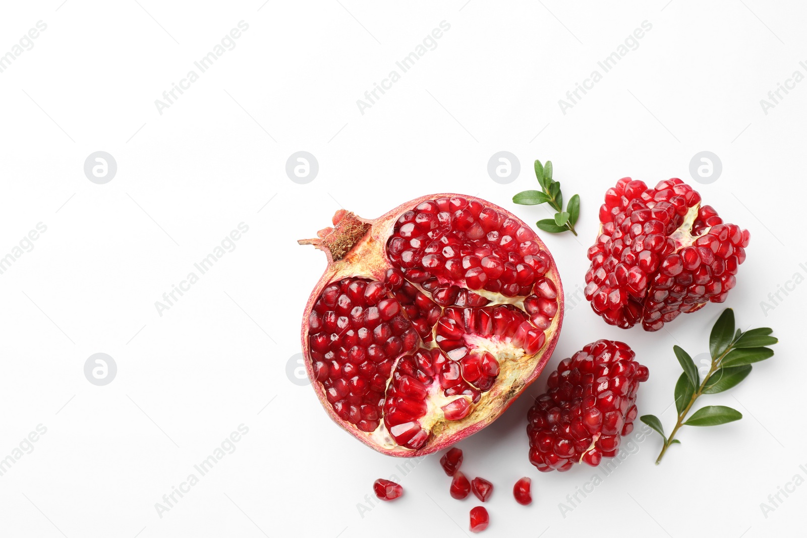 Photo of Cut fresh pomegranate and green leaves on white background, flat lay. Space for text