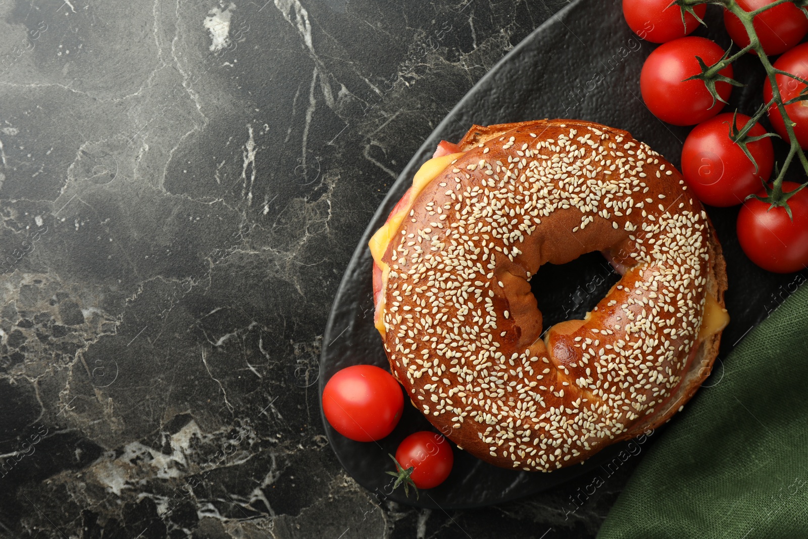 Photo of Delicious bagel with ham, cheese and tomatoes on dark marble table, top view. Space for text