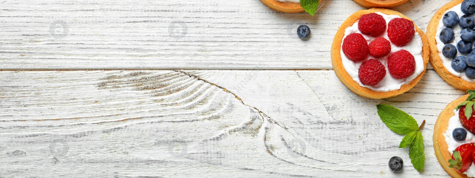 Image of Delicious tartlets with fresh berries on white wooden table, flat lay with space for text. Banner design