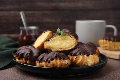 Delicious profiteroles with chocolate spread and cream on textured table, closeup