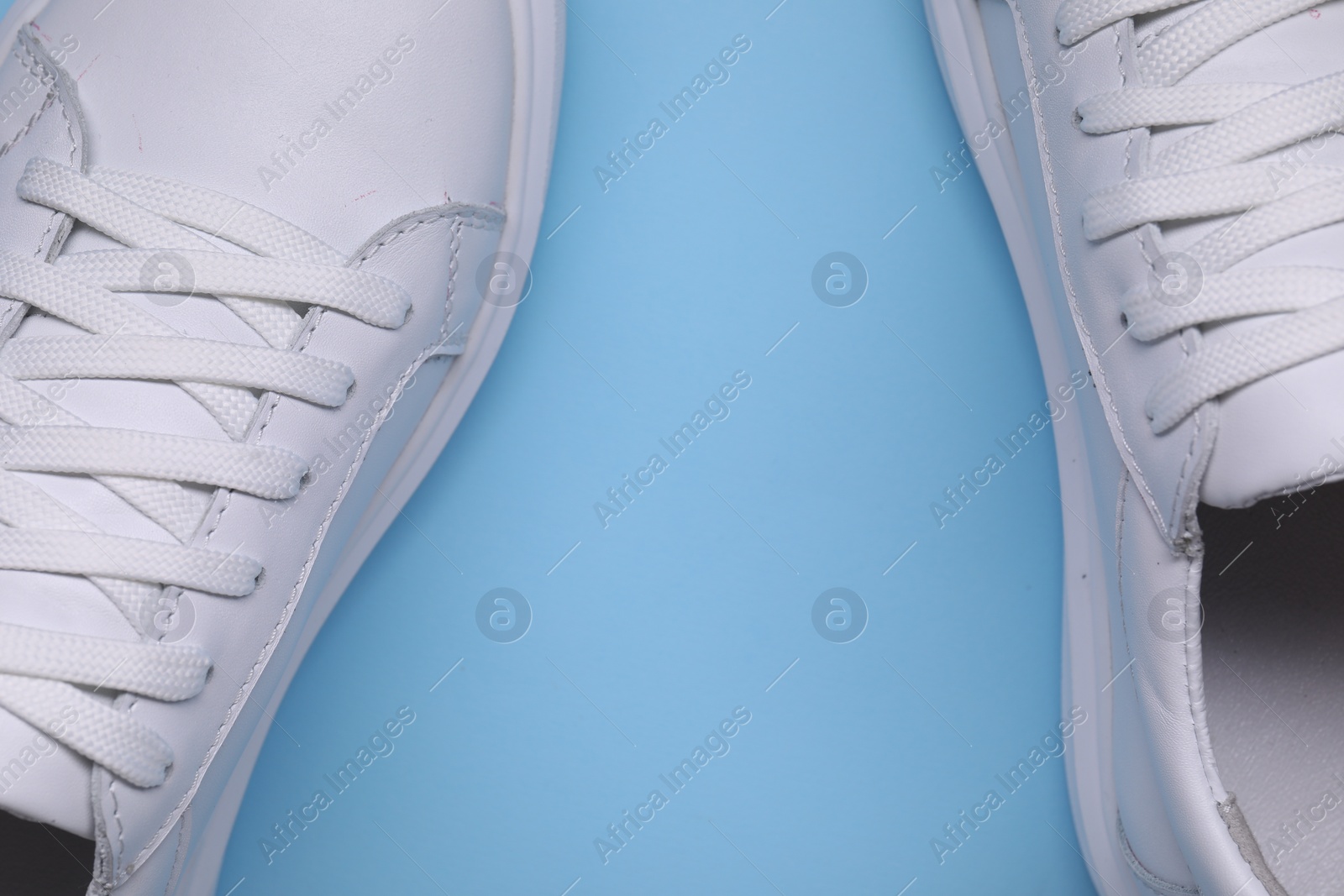 Photo of Pair of stylish white sneakers on light blue background, top view. Space for text