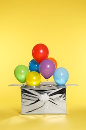 Gift box with bright air balloons on color background