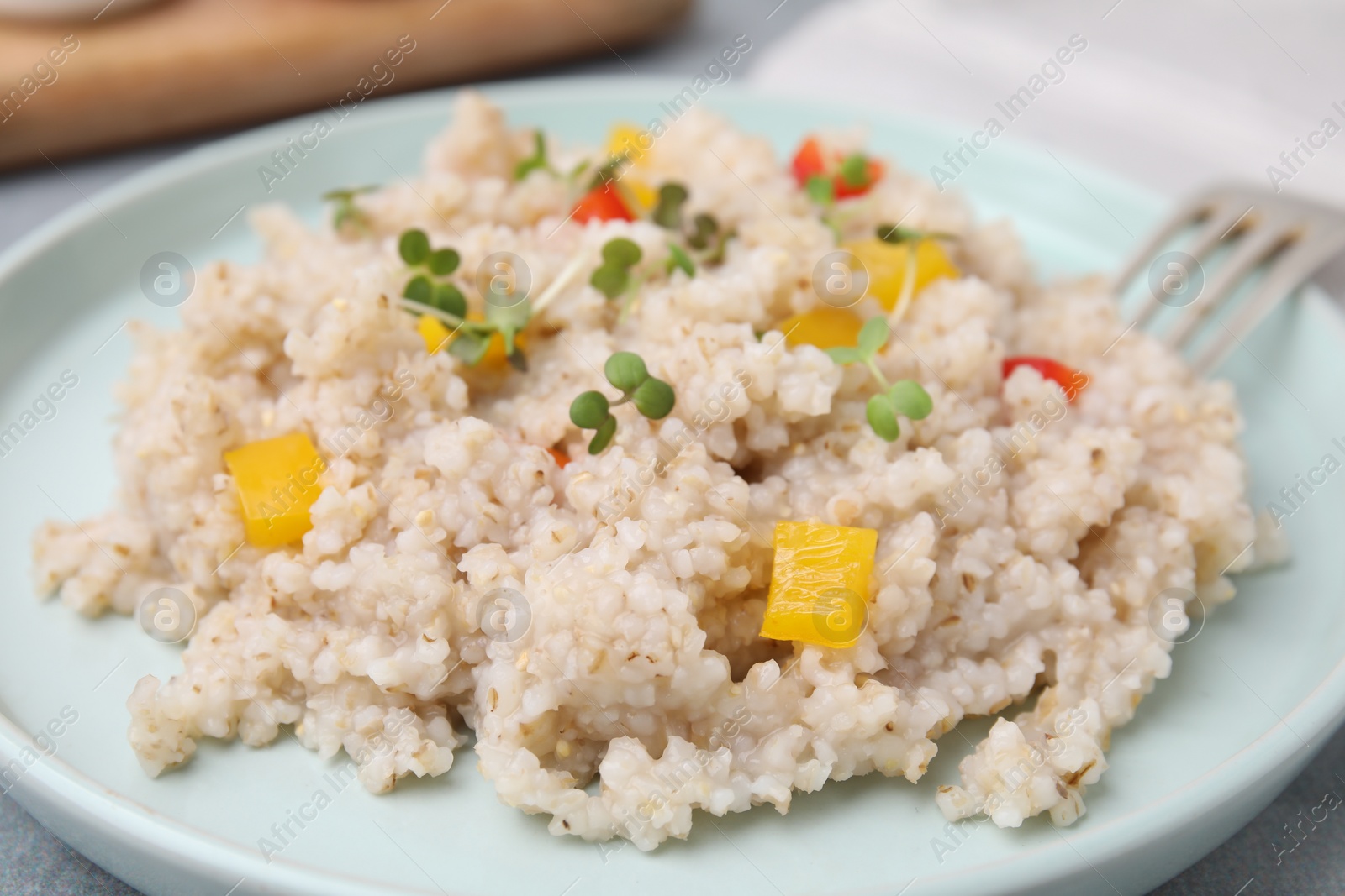 Photo of Delicious barley porridge with vegetables and microgreens on table, closeup