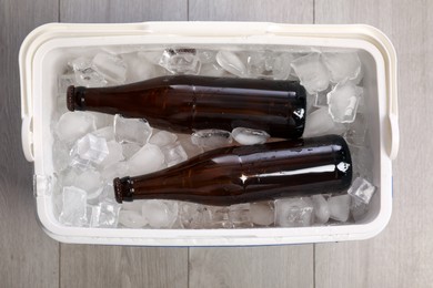 Plastic cool box with ice cubes and beer on wooden floor, top view