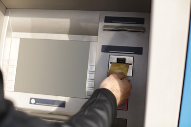 Man inserting credit card into cash machine outdoors, closeup