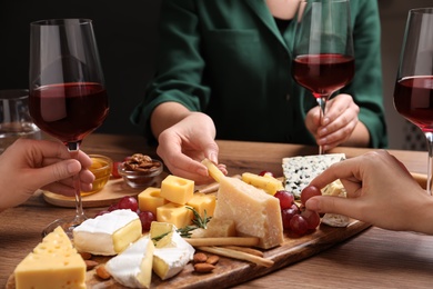 Photo of Women with cheese plate and glasses of wine at wooden table, closeup