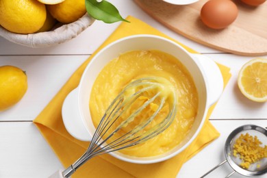 Delicious lemon curd in bowl, ingredients, whisk and sieve on white wooden table, flat lay