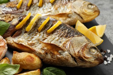 Photo of Tasty homemade roasted crucian carps served on slate plate, closeup. River fish