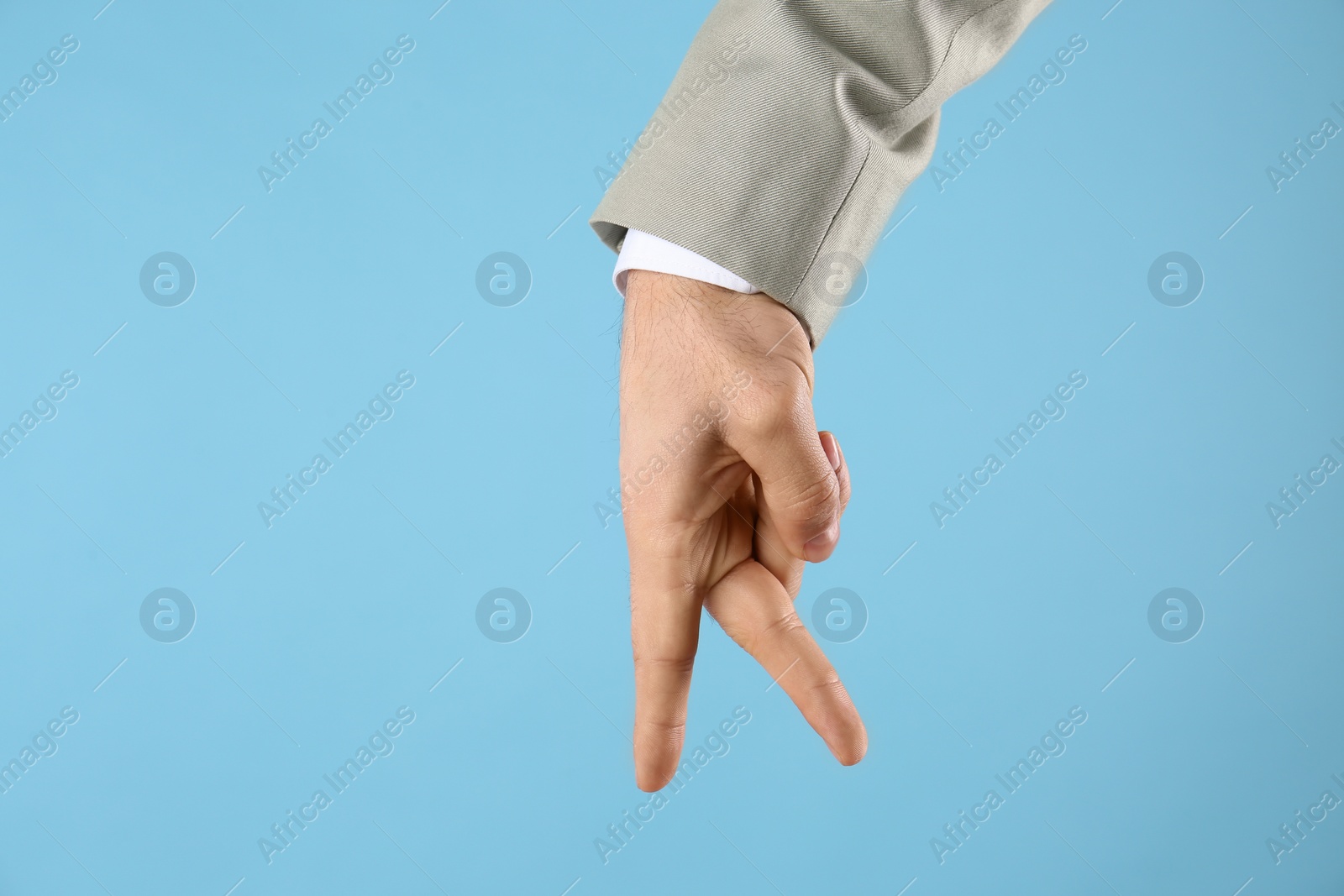 Photo of Businessman imitating walk with hand on light blue background, closeup. Finger gesture