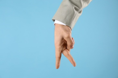 Businessman imitating walk with hand on light blue background, closeup. Finger gesture