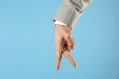 Photo of Businessman imitating walk with hand on light blue background, closeup. Finger gesture