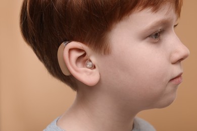 Little boy with hearing aid on pale brown background, closeup