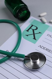Medical prescription form, stethoscope and pills on light grey background, closeup
