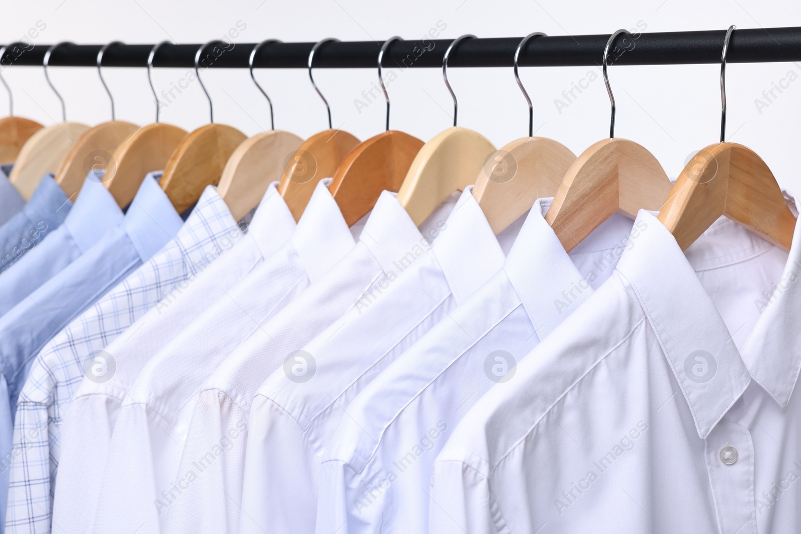 Photo of Dry-cleaning service. Many different clothes hanging on rack against white background, closeup