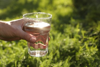 Photo of Man holding glass of fresh water outdoors, closeup. Space for text