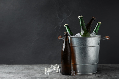 Photo of Metal bucket with beer and ice cubes on grey background. Space for text