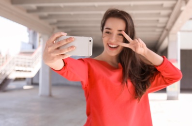 Photo of Attractive young woman taking selfie with phone outdoors