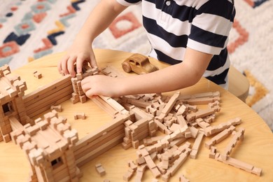 Little boy playing with wooden construction set at table indoors, closeup. Child's toy