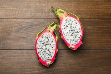 Photo of Halves of delicious dragon fruit (pitahaya) on wooden table, flat lay