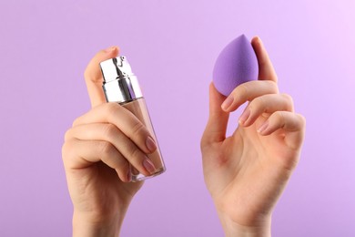 Photo of Woman with makeup sponge and skin foundation on violet background, closeup