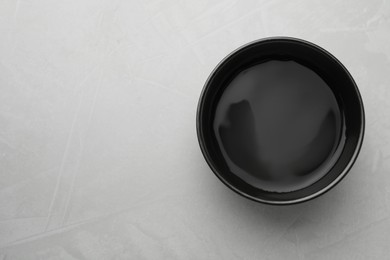 Black bowl with water on grey table, top view. Space for text