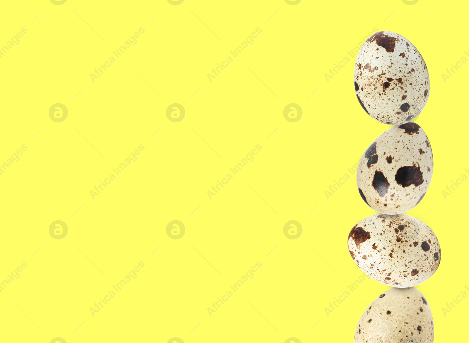 Image of Stacked speckled quail eggs on light yellow background. Space for text