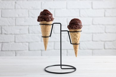 Photo of Chocolate ice cream scoops in wafer cones on white wooden table against brick wall