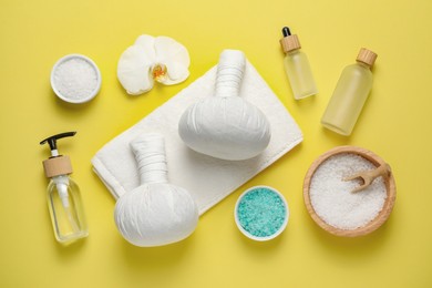 Photo of Beautiful spa composition with herbal massage bags and different care products on yellow background, flat lay