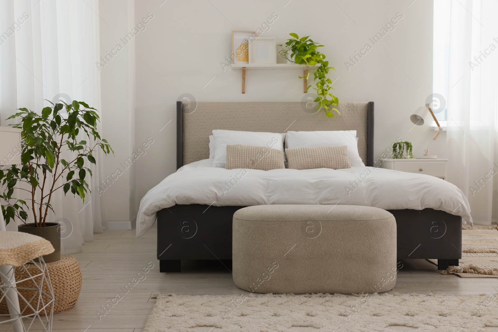 Photo of Stylish bedroom interior with large comfortable bed, ottoman and bedside table