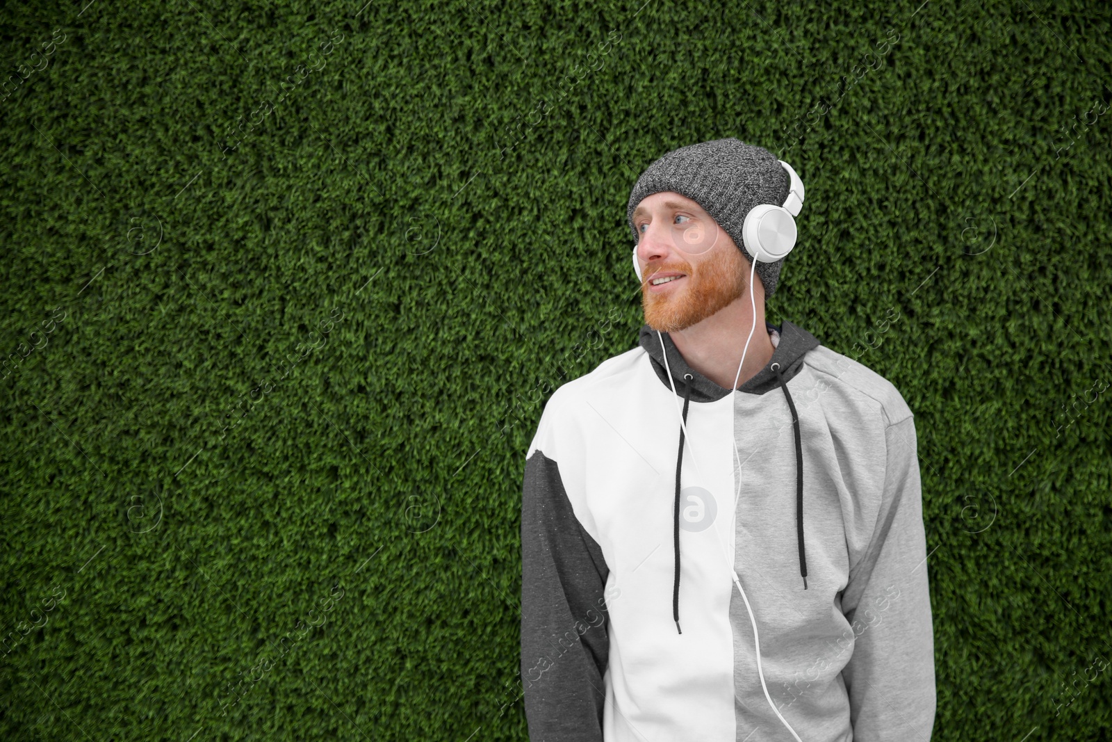 Photo of Young man listening to music with headphones near grass wall. Space for text