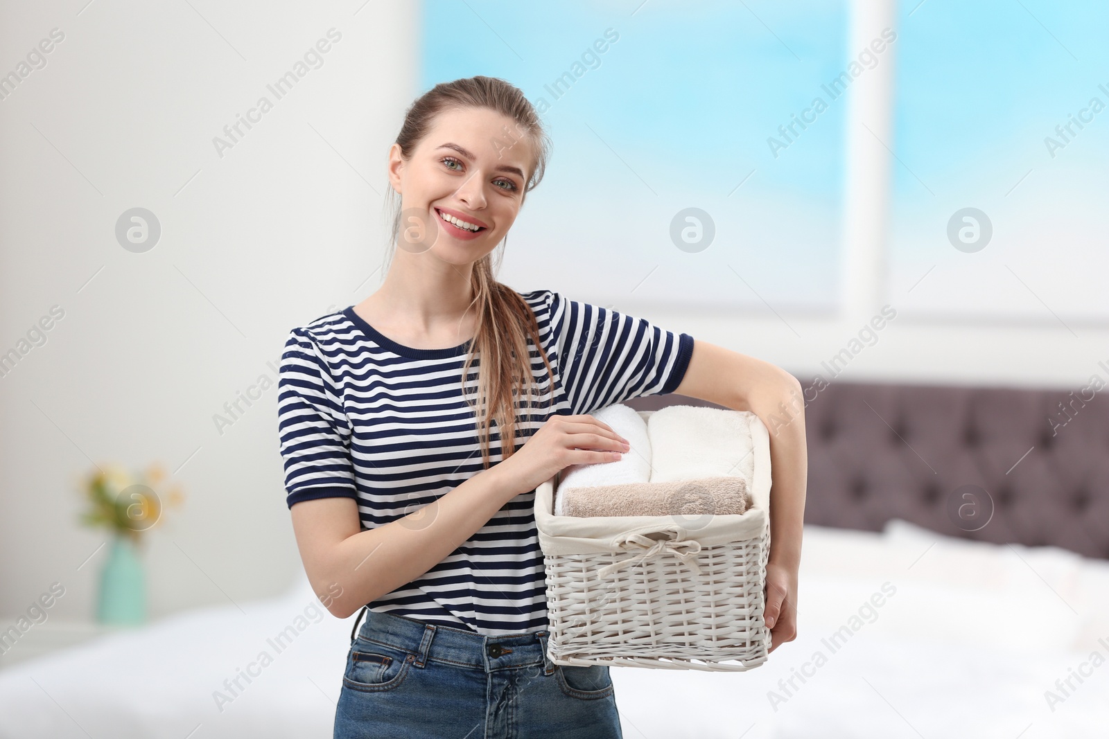 Photo of Woman holding wicker basket with folded clean towels in bedroom. Laundry day