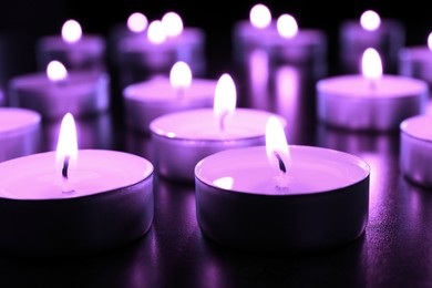 Image of Beautiful burning violet candles on black background, closeup. Funeral attributes