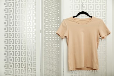 Photo of Beige t-shirt hanging on white folding screen, space for text