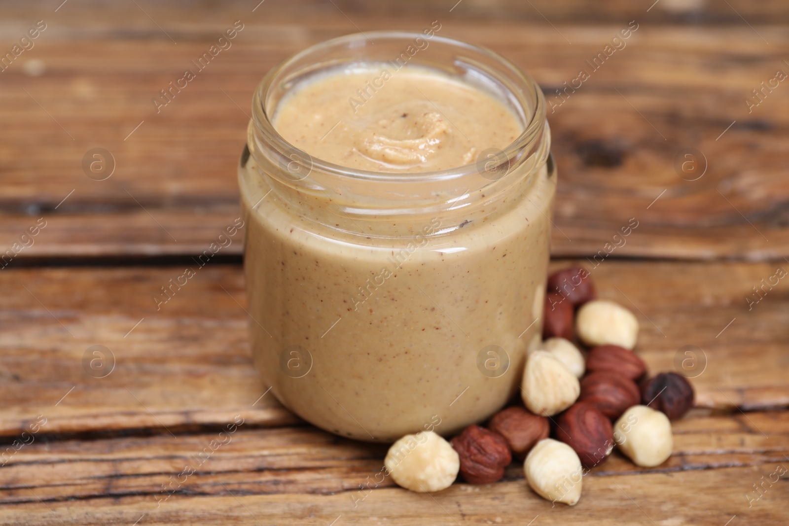 Photo of Tasty nut paste in jar and hazelnuts on wooden table, closeup