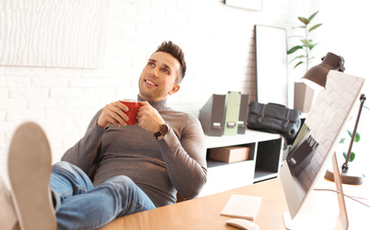 Photo of Young man with cup of drink relaxing at table in office during break