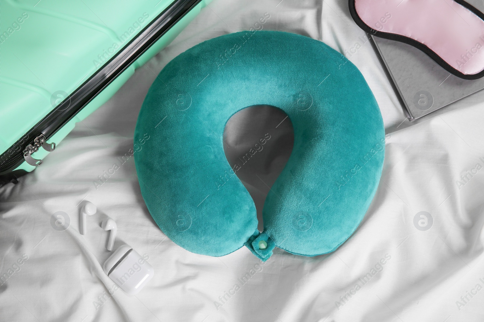 Photo of Turquoise travel pillow, suitcase, sleep mask and earphones on bed, flat lay