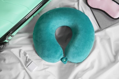 Turquoise travel pillow, suitcase, sleep mask and earphones on bed, flat lay