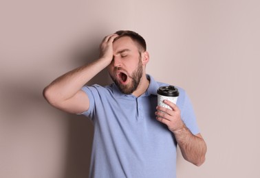 Photo of Sleepy young man with cup of coffee yawning on beige background