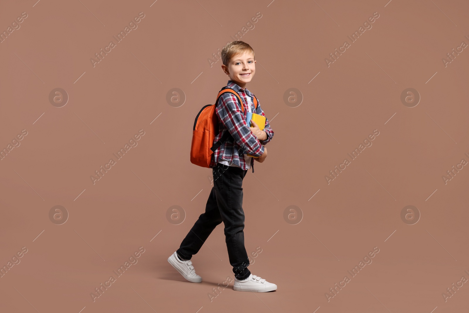 Photo of Happy schoolboy with backpack and books on brown background, space for text