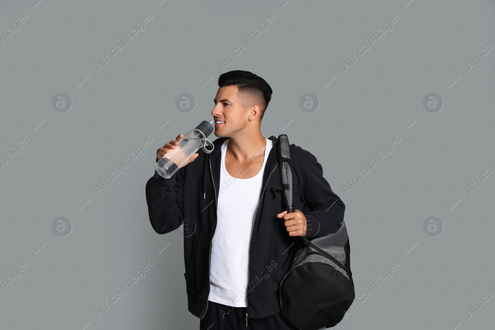 Photo of Handsome man with sports bag drinking water on grey background