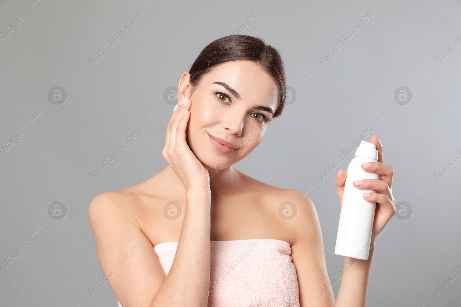 Photo of Young woman with bottle of thermal water on grey background. Cosmetic product