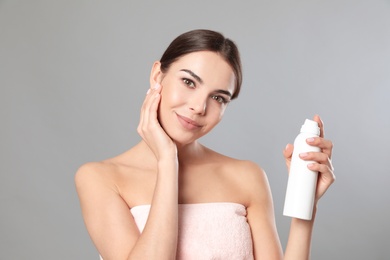 Young woman with bottle of thermal water on grey background. Cosmetic product