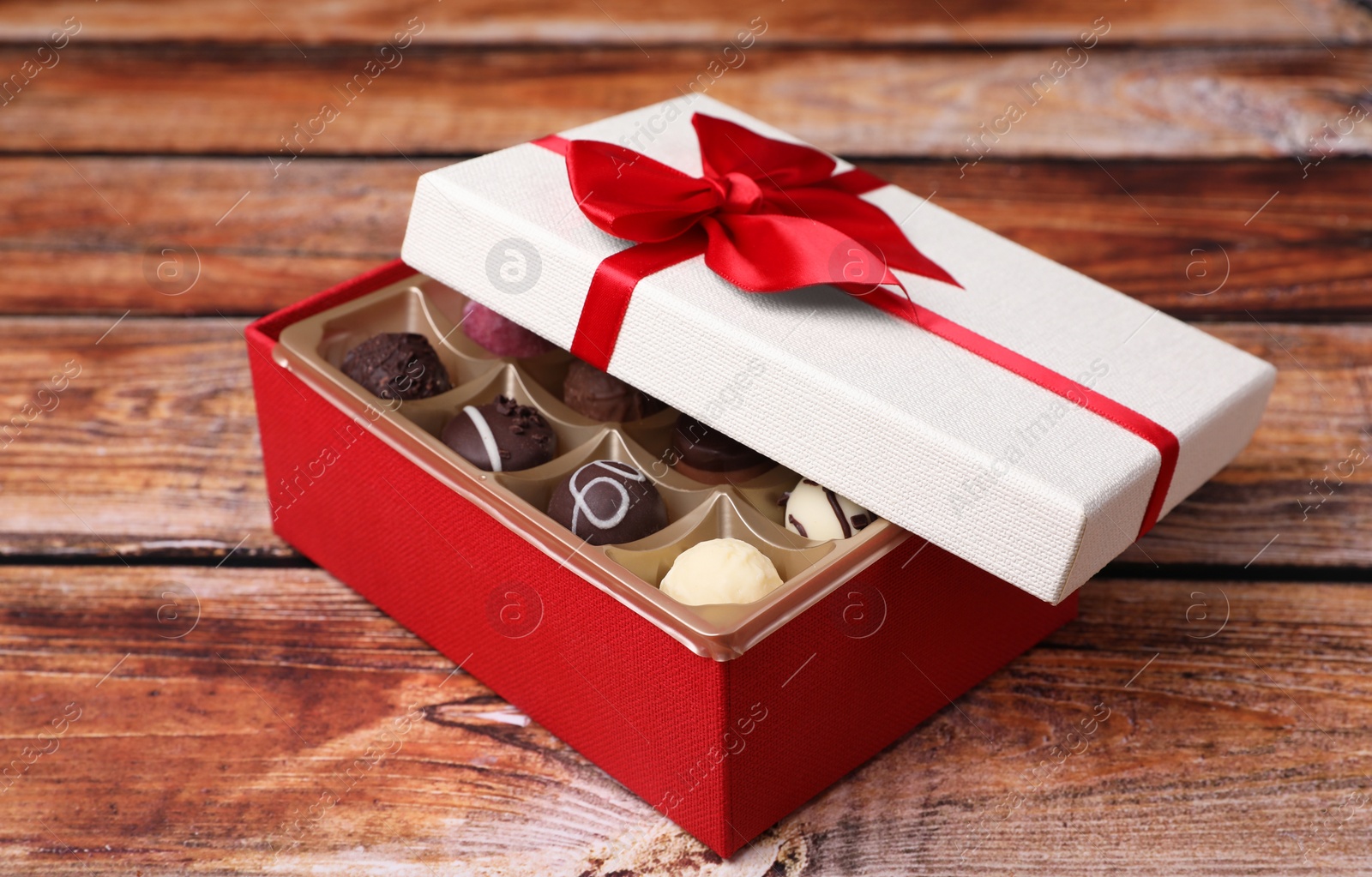 Photo of Red box with tasty chocolate candies on wooden table