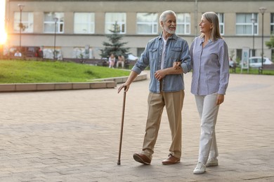 Photo of Senior man with walking cane and mature woman outdoors. Space for text