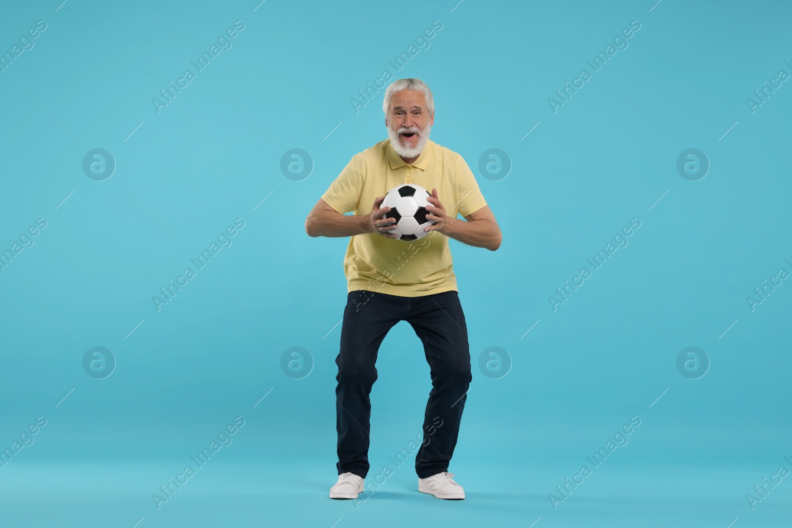 Photo of Happy senior sports fan with soccer ball on light blue background