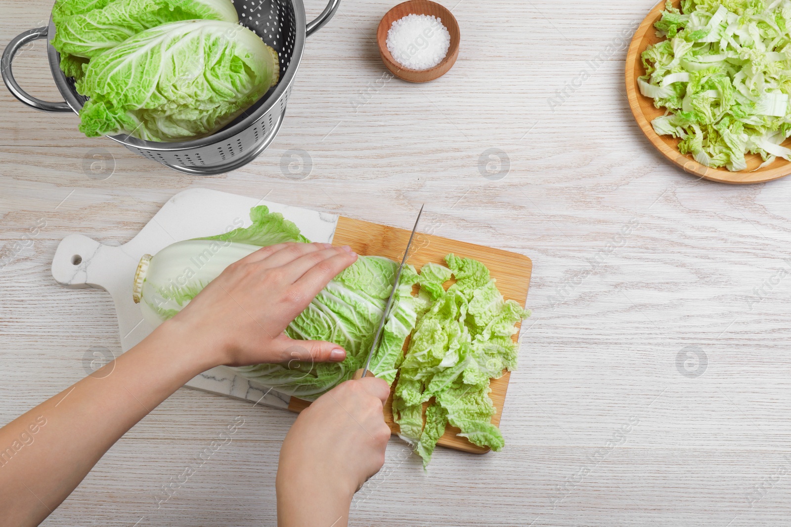 Photo of Woman cutting Chinese cabbage at white wooden kitchen table, top view