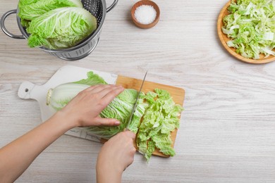 Photo of Woman cutting Chinese cabbage at white wooden kitchen table, top view