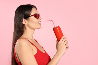 Photo of Beautiful young woman with stylish sunglasses drinking from tin can on pink background. Space for text