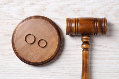 Photo of Divorce process. Gavel and wedding rings on white wooden table, flat lay