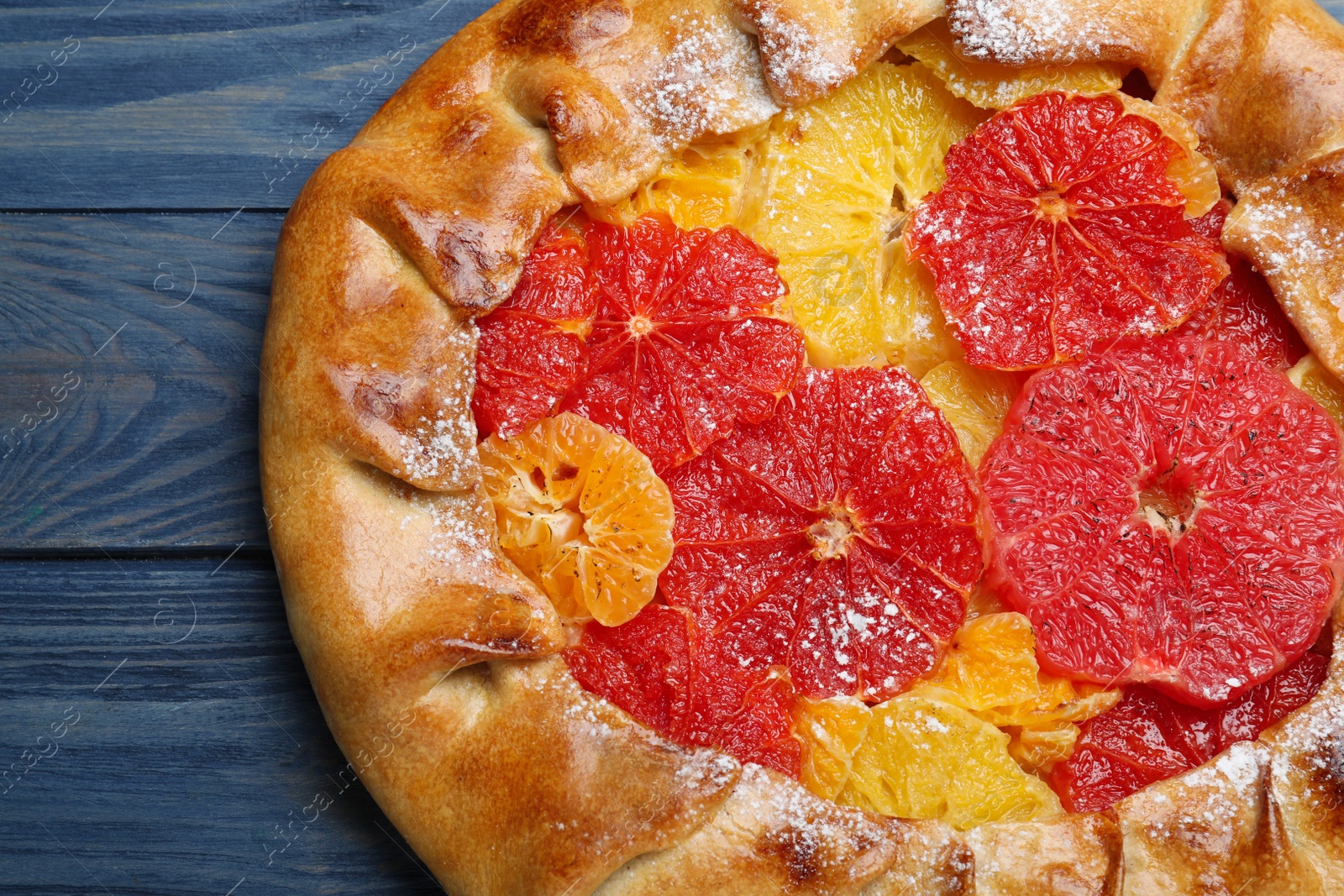 Photo of Delicious galette with citrus fruits on blue wooden table, closeup